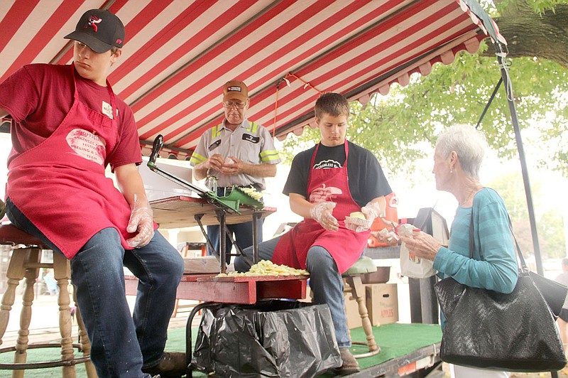 FILE PHOTO Brothers Kevin Dunn and Keelen Dunn volunteer at the apple tent at the 2021 Arkansas Apple Festival. They are giving away apples slices to Dona Biggers of Prairie Grove. Larry Luond of Lincoln is in the background, also volunteered for the day.