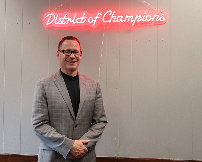 Anna Campbell/News Tribune photo: 
Jefferson City Superintendent Bryan McGraw stands next to a neon "District of Champions" sign that hangs over his desk. McGraw said the motto is intended to encourage excellence in all areas, which includes preparing students for college with Advanced Placement courses.