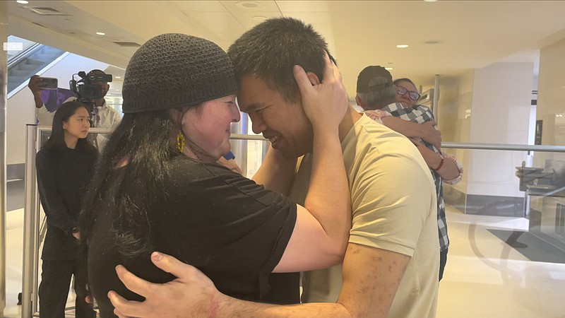 Andy Huynh, foreground, and Alex Drueke, far right, are seen hugging their loved ones after arriving at Birmingham-Shuttlesworth International Airport in Birmingham, Ala., Saturday, Sept. 24, 2022. The U.S. military veterans disappeared three months ago while fighting Russia with Ukrainian forces. They were released earlier this week by Russian-backed separatists as part of a prisoner exchange. (AP Photo/Kim Chandler)