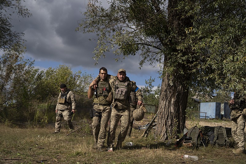 A Ukrainian serviceman helps a comrade during an evacuation of injured soldiers participating in the counteroffensive, in a region near the retaken village of Shchurove, Ukraine, Sunday, Sept. 25, 2022. (AP Photo/Leo Correa)