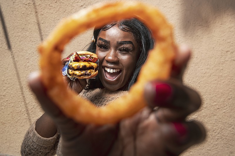 Nkechi Ahaiwe, a food influencer based in Los Angeles who runs the Instagram account @eatwhateveryouwant, is photographed May 13, 2022, in West Hollywood with food from Hollywood Burger. She is holding an onion ring in one hand and a Double VIP Cheeseburger in the other. Ahaiwe's account has more than 63,000 followers. (Mel Melcon/Los Angeles Times/TNS)