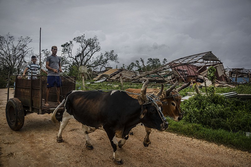 Men lead their ox cart past a tobacco warehouse smashed by Hurricane Ian in Pinar del Rio, Cuba, Tuesday, Sept. 27, 2022. Hurricane Ian tore into western Cuba as a major hurricane and left 1 million people without electricity, then churned on a collision course with Florida over warm Gulf waters amid expectations it would strengthen into a catastrophic Category 4 storm. (AP Photo/Ramon Espinosa)