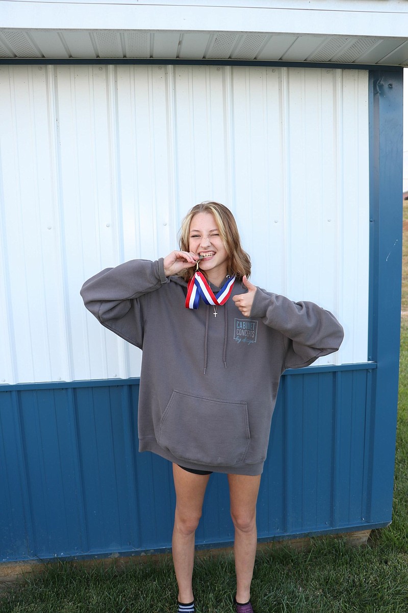 South Callaway girls cross country runner Kilea Holtmeyer bites her Show-Me Conference gold medal Wednesday at South Callaway High School in Mokane. (Contributed Photo)