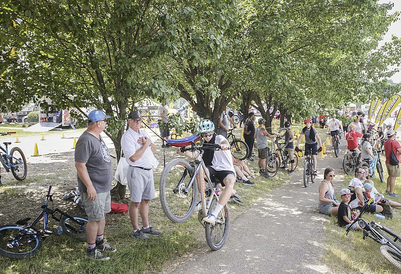 Attendees cool off in the shade as riders jump bikes over ramps, Friday, June 18, 2021 during the Bentonville Bike Fest in Bentonville. (NWA Democrat-Gazette/Charlie Kaijo)