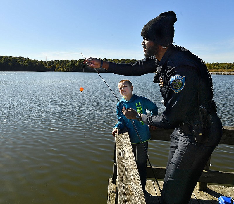 Tre Boyd, an officer with the Fayetteville Police Department, helps Declan Richards, 9, to cast a lure into the lake Thursday, Oct. 20, 2022, while helping to teach students how to fish at Lake Fayetteville. The students are participants in the Yvonne Richardson Community Center’s X-Factor program which provides physical education instruction to homeschooled students twice weekly. Visit nwaonline.com/221021Daily/ for today's photo gallery. 
(NWA Democrat-Gazette/Andy Shupe)