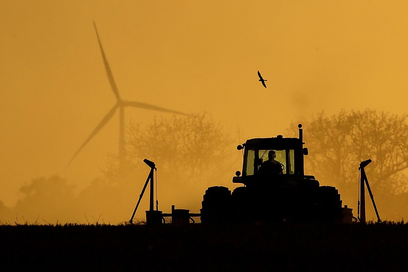 FILE - Dallas Koehn plants milo in his field as wind turbines rise in the distance on May 19, 2020, near Cimarron, Kan. The federal government announced Tuesday, Oct. 18, 2022, a program that will provide $1.3 billion in debt relief for about 36,000 farmers who have fallen behind on loan payments or face foreclosure. (AP Photo/Charlie Riedel, File)