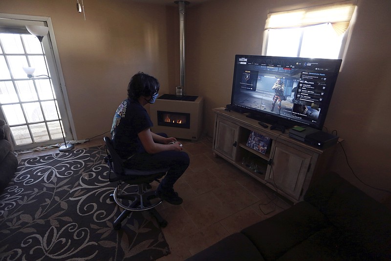 FILE - Javin Lujan Lopez, 17, a senior at Pojoaque High School, plays video games at his house, Feb. 22, 2021, in Española, N.M. In interviews with The Associated Press, close to 50 school leaders, teachers, parents and health officials reflected on decisions to keep students in extended online learning, especially during the spring semester of 2021. (AP Photo/Cedar Attanasio, File)