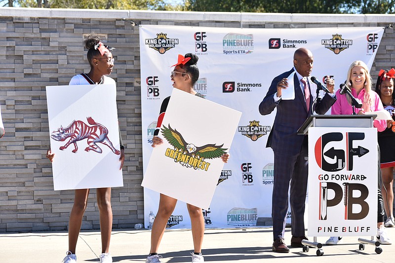 A Pine Bluff High School cheerleaders holds a Zebra logo while a White Hall High School cheerleader reveals the logo of Georgia's Greenforest-McCalep Christian Academic Center during the announcement of the 16-team King Cotton Holiday Classic field Wednesday at Pine Bluff's Main Street Plaza. Tournament director Samuel Glover, background, makes remarks along with KATV (channel 7) reporter Ansley Watson.