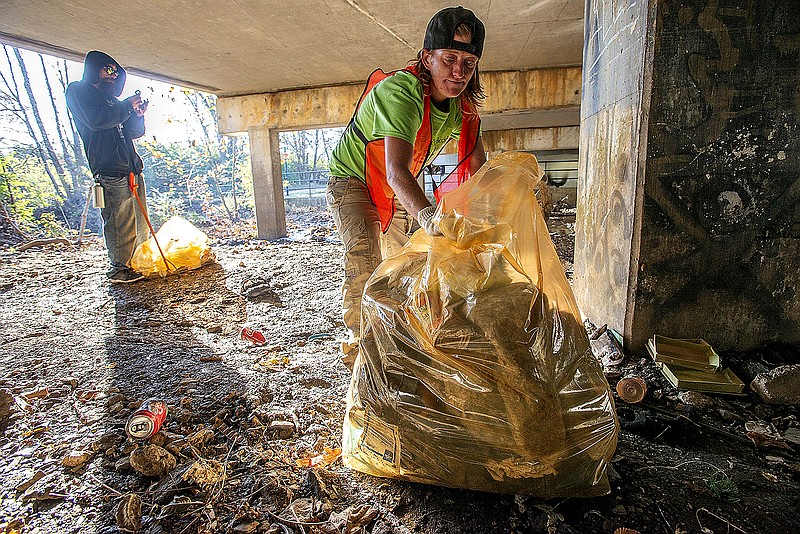 Raenee Blevins ((CQ)) fills a bag with trash Wednesday Nov. 2, 2022 under a bridge in south Fayetteville. The city partnered with Genesis Church to start the Pick Me Up pilot program in which unsheltered residents are paid to clean up campsites in South Fayetteville.  Visit nwaonline.com/221102Daily/ for today's photo gallery.  (NWA Democrat-Gazette/J.T. Wampler)