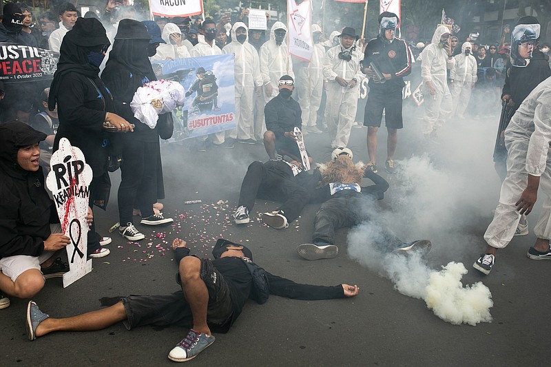 Protesters use smoke bomb as they stage an act depicting the victims of Oct. 1 soccer stampede, during a rally commemorating 40 days since the tragedy, in Malang, East Java, Indonesia, Thursday, Nov. 10, 2022. Thousands of people rallied Thursday demanding justice and a thorough investigation into those they blame for the stampede at Kanjuruhan soccer stadium that left a number of people dead after police fired tear gas at a domestic league soccer match and caused a deadly crush as spectators attempted to flee. (AP Photo/Rizki Dwi Putra)