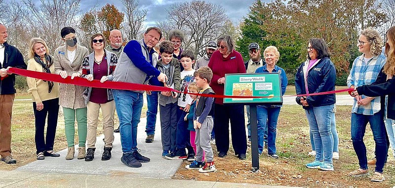 Gravette library director Karen Benson (wearing the red sweater) looks on as Samuel, Elijah, Noah and Abigail Holloway assist Gravette Mayor Kurt Maddox in cutting the ribbon at the storywalk in Hiwasse Park. Others present at the ceremony held Nov. 7 included Chamber of Commerce president Steve Harari; library assistants Artemis Edmisten and Brittany Mangold; Police Chief Chuck Skaggs; Zina Weihe, a member of the Hiwasse Committee; and members of the Hiwasse community.
(Submitted Photo/Greater Gravette Chamber of Commerce)