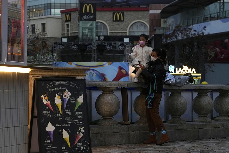 A woman and child wearing masks to curb COVID spread, pass by a deserted mall in Beijing, Tuesday, Nov. 22, 2022. More than 253,000 coronavirus cases have been found in China in the past three weeks and the daily average is rising, the government said Tuesday, adding to pressure on officials who are trying to reduce economic damage by easing controls that confine millions of people to their homes. (AP Photo/Ng Han Guan)