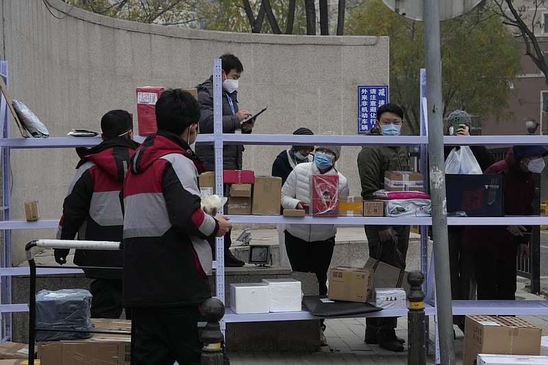 Residents wait for their deliveries behind shelves outside a community in Beijing, Thursday, Nov. 24, 2022. China is expanding lockdowns, including in a central city where factory workers clashed this week with police, as its number of COVID-19 cases hit a daily record. (AP Photo/Ng Han Guan)