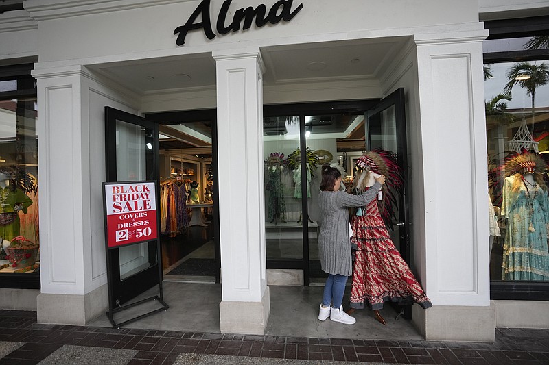 An employee sets up a display, outside a clothing stores advertising sales ahead of Black Friday and the Thanksgiving holiday, Monday, Nov. 21, 2022, in Miami. Retailers are ushering in the start of the holiday shopping season on the day after Thanksgiving, preparing for the biggest crowds since 2019. (AP Photo/Rebecca Blackwell)