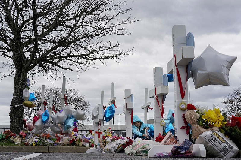 A woman ties balloons to a cross in a makeshift memorial in the parking lot of a Walmart in Chesapeake, Va., Monday, Nov. 28, 2022, for the six people killed at this Walmart when a manager opened fire with a handgun before an employee meeting last week. (AP Photo/Carolyn Kaster)
