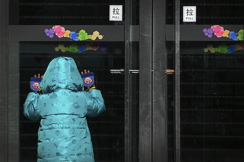 A child peeps into a shuttered shopping mall as part of COVID-19 controls Thursday, Dec. 1, 2022, in Beijing. More cities eased anti-virus restrictions as Chinese police tried to head off protests Thursday while the ruling Communist Party prepared for the high-profile funeral of the late leader Jiang Zemin. (AP Photo/Andy Wong)