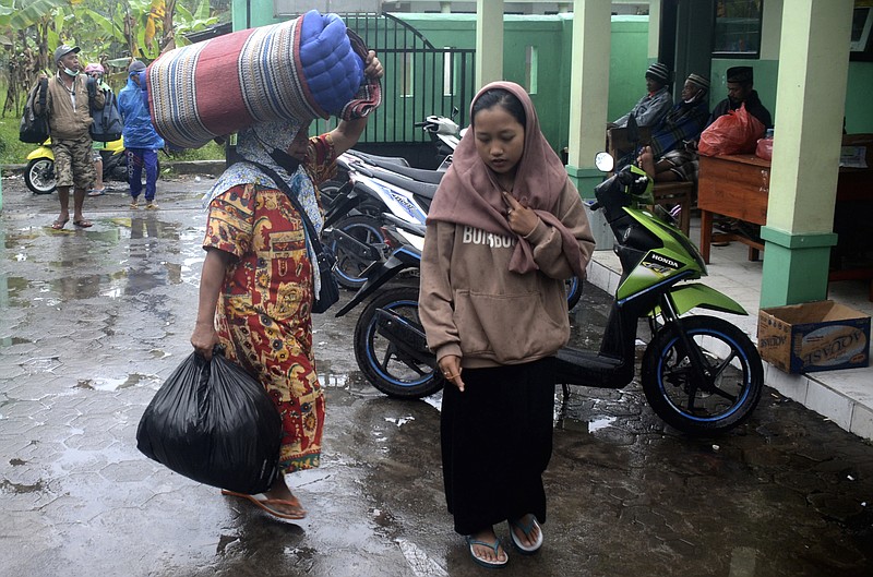 People carry their belongings as they arrive at a school turned into temporary shelter for those affected by the eruption of Mount Semeru, in Lumajang, East Java, Indonesia, Sunday, Dec. 4, 2022. Indonesia's highest volcano on its most densely populated island released searing gas clouds and rivers of lava Sunday in its latest eruption. (AP Photo/Hendra Permana)