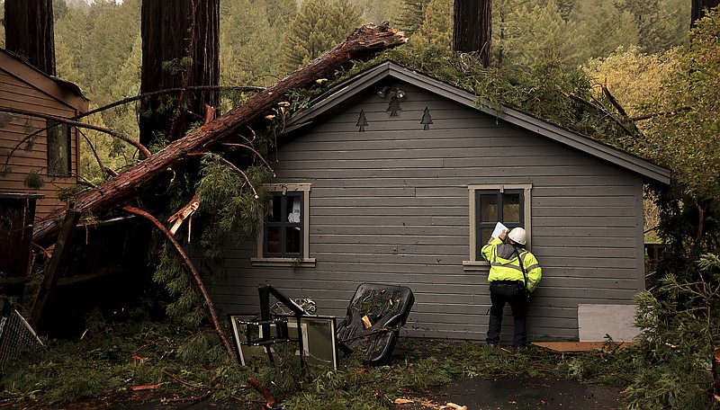 Scott Lapinski, a fire inspector with Sonoma County Fire Prevention and Hazmat Division, peers inside a building for interior damage, while inspecting its structural integrity on River Blvd in Monte Rio, Calif., Saturday, Dec. 10, 2022. No one at the home was injured. A potent winter storm is battering the west coast. (Kent Porter/The Press Democrat via AP)