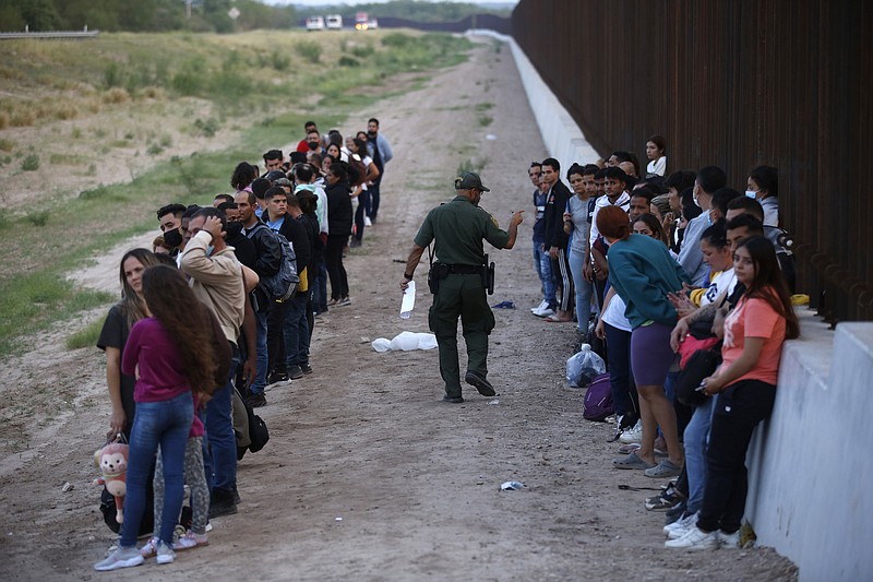 ARCHIVO - Un grupo de migrantes permanecen junto al muro de la frontera con México mientras un agente fronterizo los cuenta, el sábado 21 de mayo de 2022, en Eagle Pass, Texas. (AP Foto/Darío López-Mills, archivo)