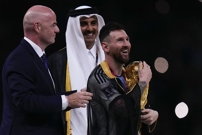 Argentina's Lionel Messi holds up the trophy flanked by FIFA President Gianni Infantino and The Emir of Qatar Sheikh Tamim bin Hamad Al Thani after winning the World Cup final soccer match between Argentina and France at the Lusail Stadium in Lusail, Qatar, Sunday, Dec.18, 2022. (AP Photo/Manu Fernandez)