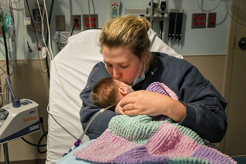 Lester Graham/Kaiser Health News photo: Caitlyn Houston kisses her infant daughter, Parker, as they wait in the emergency department for a hospital bed to open up at Corewell Health Helen DeVos Children's Hospital in Grand Rapids, Michigan. "There's so many kids in here that they have to take the ones that are really bad," Houston says.