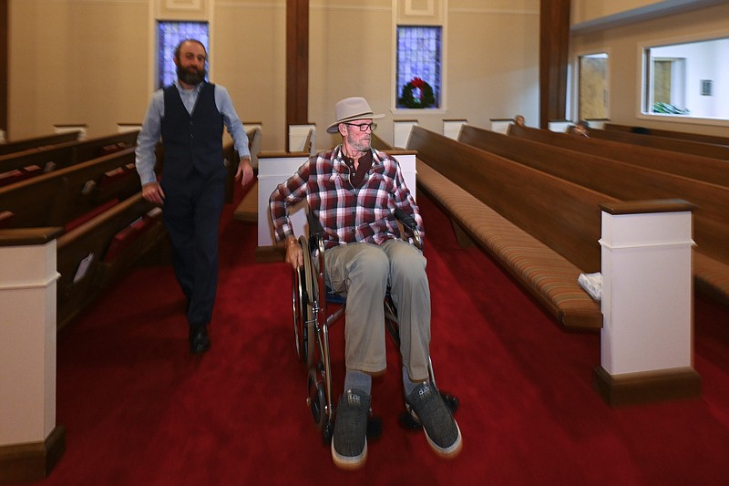 Jerry Lamb, who has a spine condition, talks to Pastor Adam Kelchner at Camden First United Methodist Church Thursday, Dec. 8, 2022, in Camden, Tenn. The church at the urging of the pastor recently had a couple pews cut in half so Jerry, and anyone else who uses a wheelchair, walker or other aid, can still sit with the rest of the congregation. (AP Photo/John Amis)