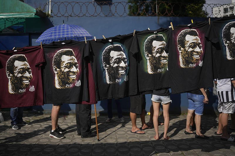 Shirts featuring Pele hang for sale where people wait in line to enter Vila Belmiro stadium where the late Brazilian soccer great lies in state in Santos, Brazil, Monday, Jan. 2, 2023. (AP Photo/Matias Delacroix)