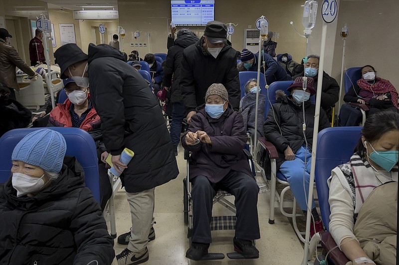 A man pushes an elderly woman past patients receiving intravenous drips in the emergency ward of a hospital, Tuesday, Jan. 3, 2023. As the virus continues to rip through China, global organizations and governments have called on the country start sharing data while others have criticized its current numbers as meaningless. (AP Photo/Andy Wong)