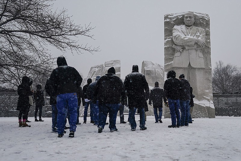 Visitors look to the Martin Luther King, Jr. Memorial as snow falls in Washington, Sunday, Jan. 16, 2022. Ceremonies scheduled for the site on Monday, to mark the Martin Luther King, Jr. national holiday, have been canceled because of the weather. (AP Photo/Carolyn Kaster)