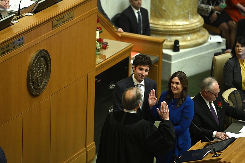 The Honorable John Dan Kemp, Chief Justice of the Arkansas Supreme Court, left, swears Sarah Huckabee Sanders into office with her Husband, Bryan, on the floor of the Arkansas House of Representatives on Tuesday, Jan. 10, 2023. (Arkansas Democrat-Gazette/Stephen Swofford)