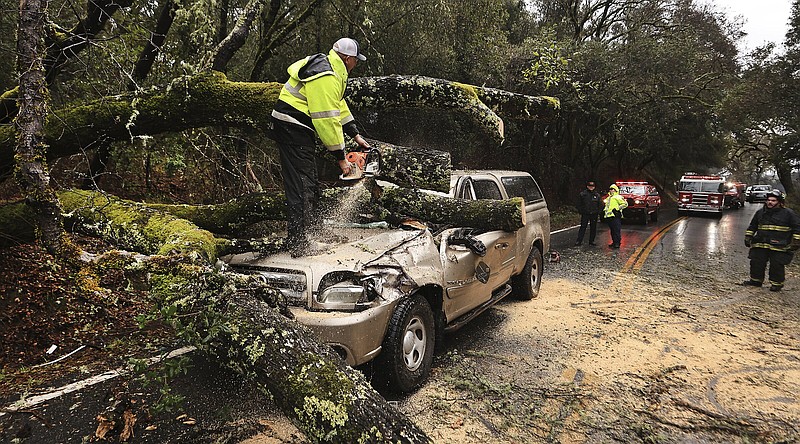 Hopland Volunteer Fire Department chief Mitch Franklin cuts away a large oak tree that fell on a vehicle, moderately injuring the driver on Old River Road, north of Hopland, Calif., in Mendocino County, Saturday, Jan. 14, 2023. Storm-battered California got more wind, rain and snow on Saturday, raising flooding concerns, causing power outages and making travel dangerous. (Kent Porter/The Press Democrat via AP)