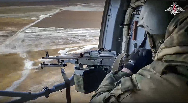 In this handout photo taken from video released by Russian Defense Ministry Press Service on Tuesday, Jan. 17, 2023, a Russian soldier points a gun from a Russian military helicopter as it flies over an undisclosed location in Ukraine. (Russian Defense Ministry Press Service photo via AP)