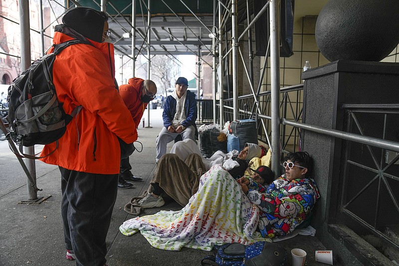 Recent immigrants to the United States lie on the sidewalk with their belongings as they talk to city officials in front of the Watson Hotel in New York, Monday, Jan. 30, 2023. The immigrants, mostly from Venezuela and other Latin American countries, had been living in the hotel until recently, when they were told to leave the temporary shelter. (AP Photo/Seth Wenig)