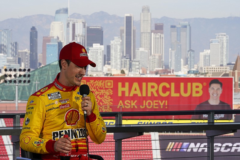 NASCAR Cup Series driver Joey Logano (22) speaks to reporters ahead of practice sessions before a NASCAR exhibition auto race at Los Angeles Memorial Coliseum, Saturday, Feb. 4, 2023, in Los Angeles. An advertisement for HairClub is shown on a sign in the stadium. Logano recently used HairClub after struggling with alopecia. (AP Photo/Ashley Landis)