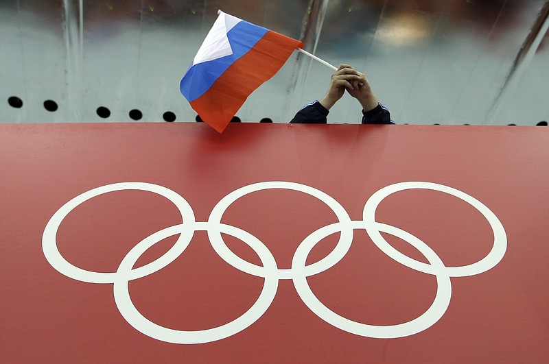 FILE - A Russian flag is held above the Olympic Rings at Adler Arena Skating Center during the Winter Olympics in Sochi, Russia on Feb. 18, 2014. Russia and its ally Belarus have been invited to compete at the Asian Games in the next step to qualify athletes for next year’s Paris Olympics. The arrangement has been brokered by the International Olympic Committee. The IOC indicated on Wednesday that it favours allowing Russians to compete at the 2024 Olympics as neutral athletes. (AP Photo/David J. Phillip, File)