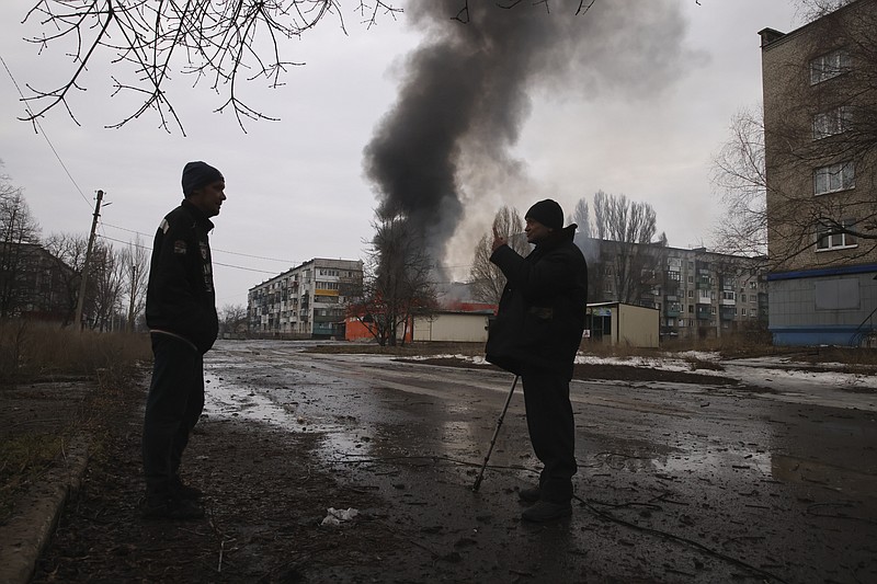 Local residents talk against the background of a building burning after the Russian shelling in the town of Chasiv Yar, the site of the heaviest battles with the Russian troops, Donetsk region, Ukraine, Monday, Feb. 27, 2023. (AP Photo/Yevhen Titov)