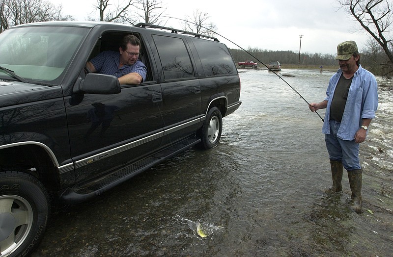 Ronnie Moore hooks a small bass in the road while talking to Kevin Dillion who had just driven north on flooded Grassy Lake Road on March 15, 2002. (Democrat-Gazette file photo)