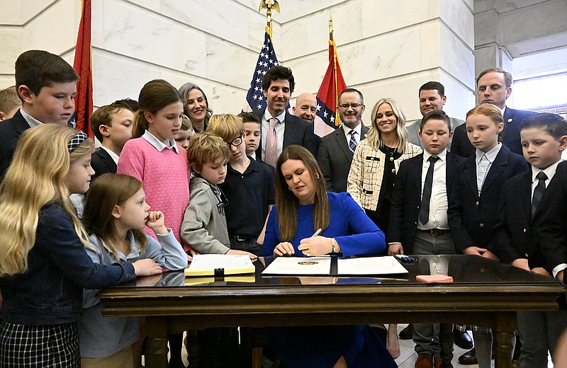 Gov. Sarah Huckabee Sanders (center) signs the LEARNS act into law during a signing ceremony in the second floor rotunda of the Arkansas state Capitol on Wednesday, March 8, 2023. Sanders was surrounded by her family, state representatives, and children from Calvary Academy in North Little Rock. (Arkansas Democrat-Gazette/Stephen Swofford)