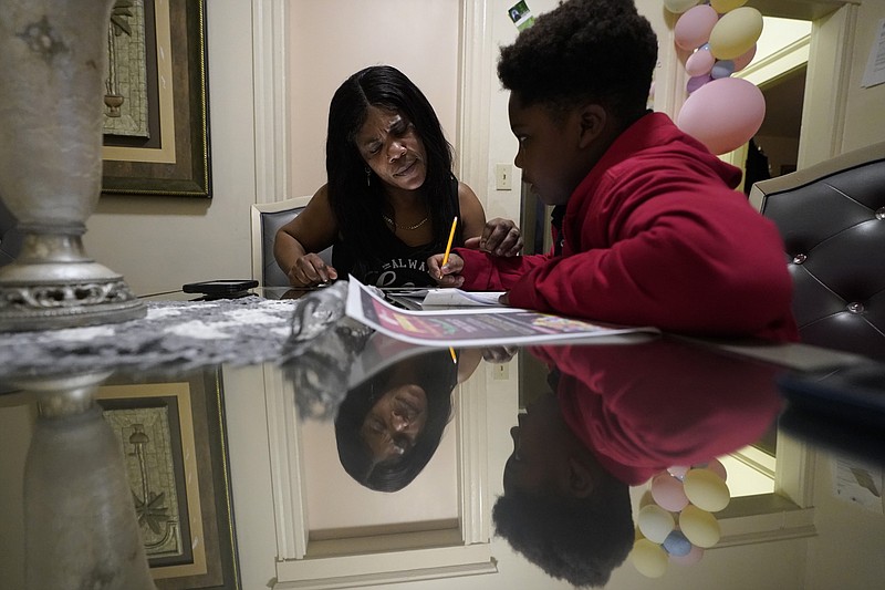 Evena Joseph, left, assists her son J. Ryan Mathurin, 9, as he does his homework, Thursday, Dec. 22, 2022, at their home, in Boston. (AP Photo/Steven Senne)