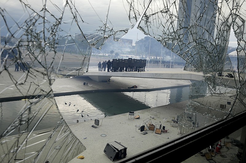 FILE - Police stand on the other side of a window at Planalto Palace that was shattered by supporters of Brazil's former President Jair Bolsonaro, after they stormed the official workplace of the President Luiz Inacio Lula da Silva, in Brasilia, Brazil, Jan. 8, 2023. Sources in the army and defense ministry, told The Associated Press they don't see any evidence of another uprising against Lula’s government in the near term, adding the high command has performed its regular duties without question. (AP Photo/Eraldo Peres, File)