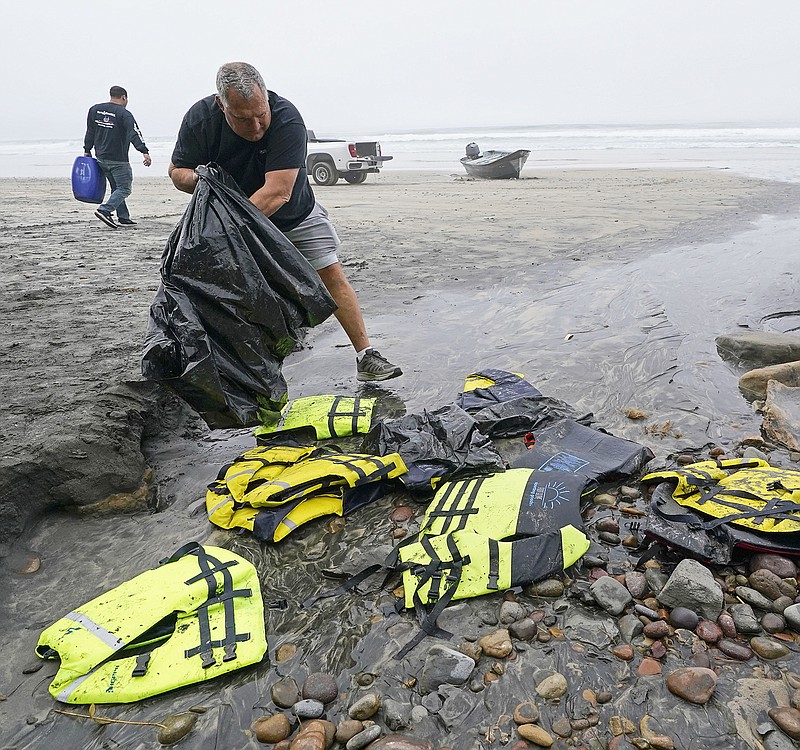 Boat salvager Robert Butler, front, picks up life preservers in front of one of two boats sitting on Blacks Beach, Sunday, March 12, 2023, in San Diego. Authorities say multiple people were killed when two suspected smuggling boats overturned off the coast San Diego, and crews were searching for additional victims. (AP Photo/Gregory Bull)