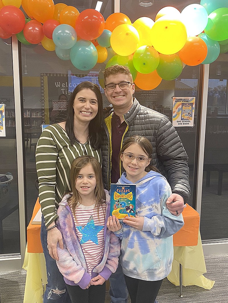 Submitted photo Ashlyn Thornton, a fifth grader at Prairie Grove Middle School, holds the book, "Escape from Mr. Lemoncello’s Library," with her parents Zach and Maddie Thornton and younger sister, Harper. Middle school students and their families read this book together at home for the school's reading initiative called One School, One Book.