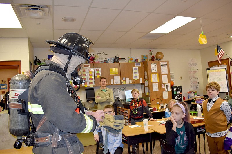 Rachel Dickerson/The Weekly Vista Bella Vista Firefighter Jayson Steeley adds gloves to the rest of his firefighting gear to show students at Cooper Elementary what a firefighter would look like while fighting a fire. Steeley and other firefighters were among those who presented during career day at the school on March 17.