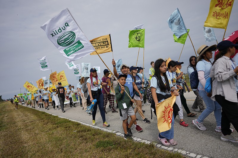 Gelder Perez, 10, center, carries a protest flag as he walks with his uncle Leonel Perez, center right, on the first day of a five-day trek aimed at highlighting the Fair Food Program, in an effort to pressure retailers to leverage their purchasing power to improve conditions for farmworkers, Tuesday, March 14, 2023, in Pahokee, Fla. The younger Perez, who was on a school break, said he planned to try to walk the whole 45-mile trek along with his uncle, who worked 15 seasons on watermelon farms before becoming an organizer with the Coalition of Immokalee Workers.  (AP Photo/Rebecca Blackwell)