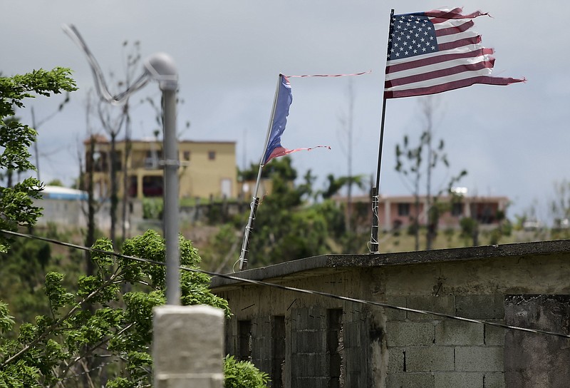 FILE -  Deteriorated U.S. and Puerto Rico flags fly on a roof eight months after the passing of Hurricane Maria in the Barrio Jacana Piedra Blanca area of Yabucoa, a town where many continue without power in Puerto Rico, May 16, 2018. Puerto Rico started in 2022 permanent repairs on an aging power grid razed by Hurricane Maria, a Category 4 storm that struck the island in September 2017. Since then, power outages have become a common occurrence, disrupting daily life. (AP Photo/Carlos Giusti, File)