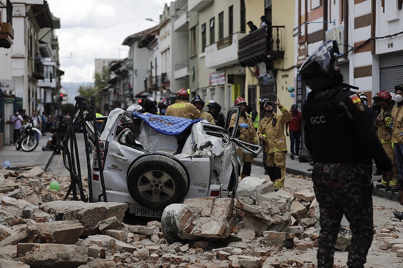 A police officer looks up next to a car crushed by debris Saturday, March 18, 2023, after an earthquake shook Cuenca, Ecuador. (AP Photo/Xavier Caivinagua)