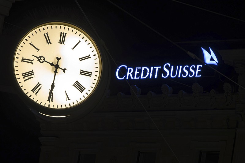 The illuminated logo of Swiss bank Credit Suisse is seen behind a clock at the banks headquarters at Paradeplatz on Saturday, March 18, 2023, in Zurich, Switzerland. (Michael Buholzer/Keystone via AP)