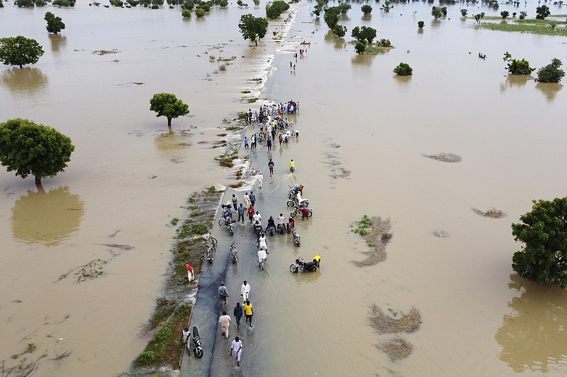 FILE - People walk through floodwaters after heavy rainfall in Hadeja, Nigeria, Sept 19, 2022. Publication of a major new United Nations report on climate change is being held up by a battle between rich and developing countries over emissions targets and financial aid to vulnerable nations. (AP Photo, File)