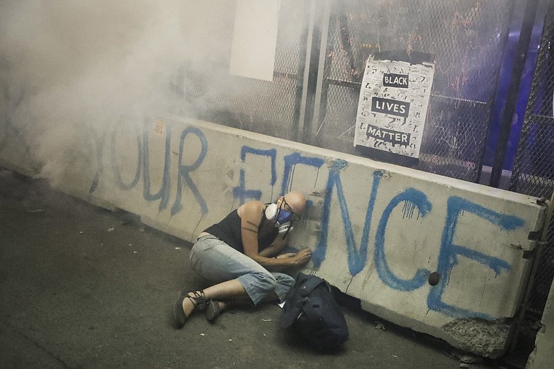 A demonstrator hides under a barrier as federal officers release tear gas during a Black Lives Matter protest at the Mark O. Hatfield United States Courthouse on July 29, 2020, in Portland, Ore. More than 119,000 people have been injured by tear gas and other chemical irritants around the world since 2015 and some 2,000 suffered injuries from "less lethal" impact projectiles, according to a new report released Wednesday, March 22, 2023. (AP Photo/Marcio Jose Sanchez, File)