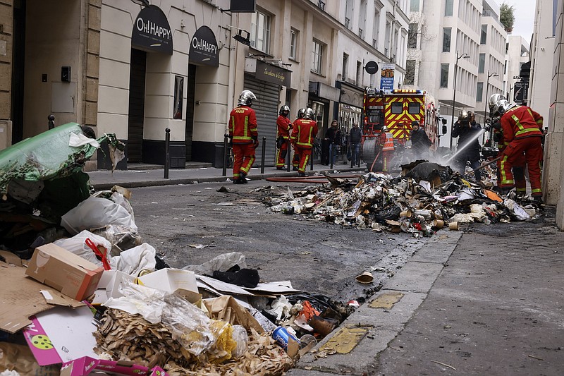 Firemen controlling the remains of a garbage fire from last night protests against the retirement bill in Paris, Friday, March 24, 2023. French President Macron's office says state visit by Britain's King Charles III is postponed amid mass strikes and protests. (AP Photo/Thomas Padilla)